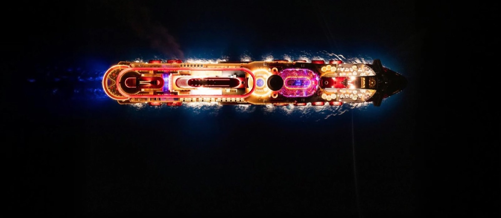 A modern cruise ship lit up at night, seen from above on dark open water