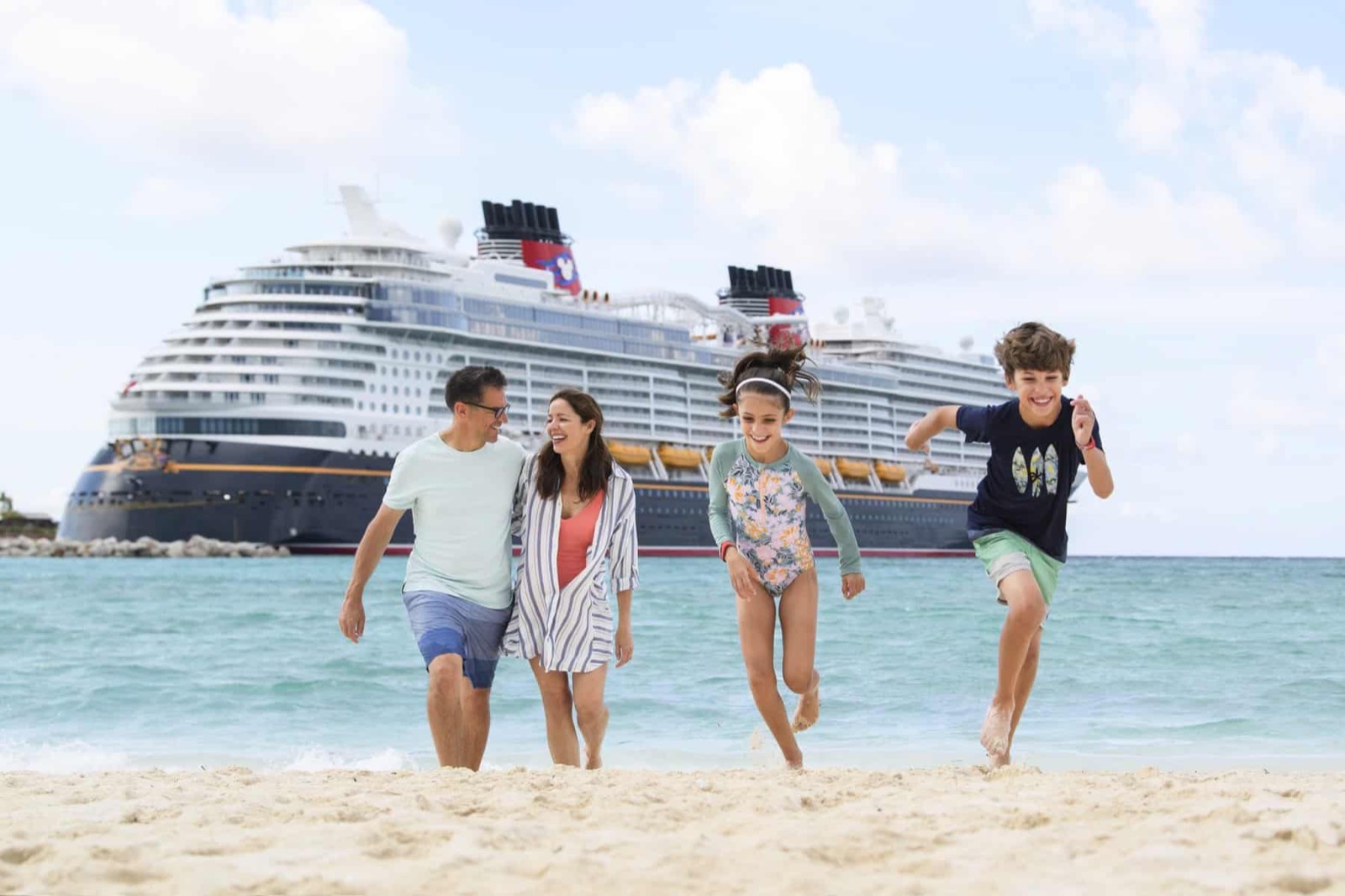 A Disney Cruise Line ship anchored off a white-sand beach as a family plays in the surf