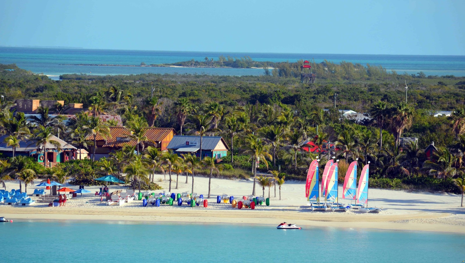 A turquoise Bahamian beach with palms and sailboats at a private-island cruise stop