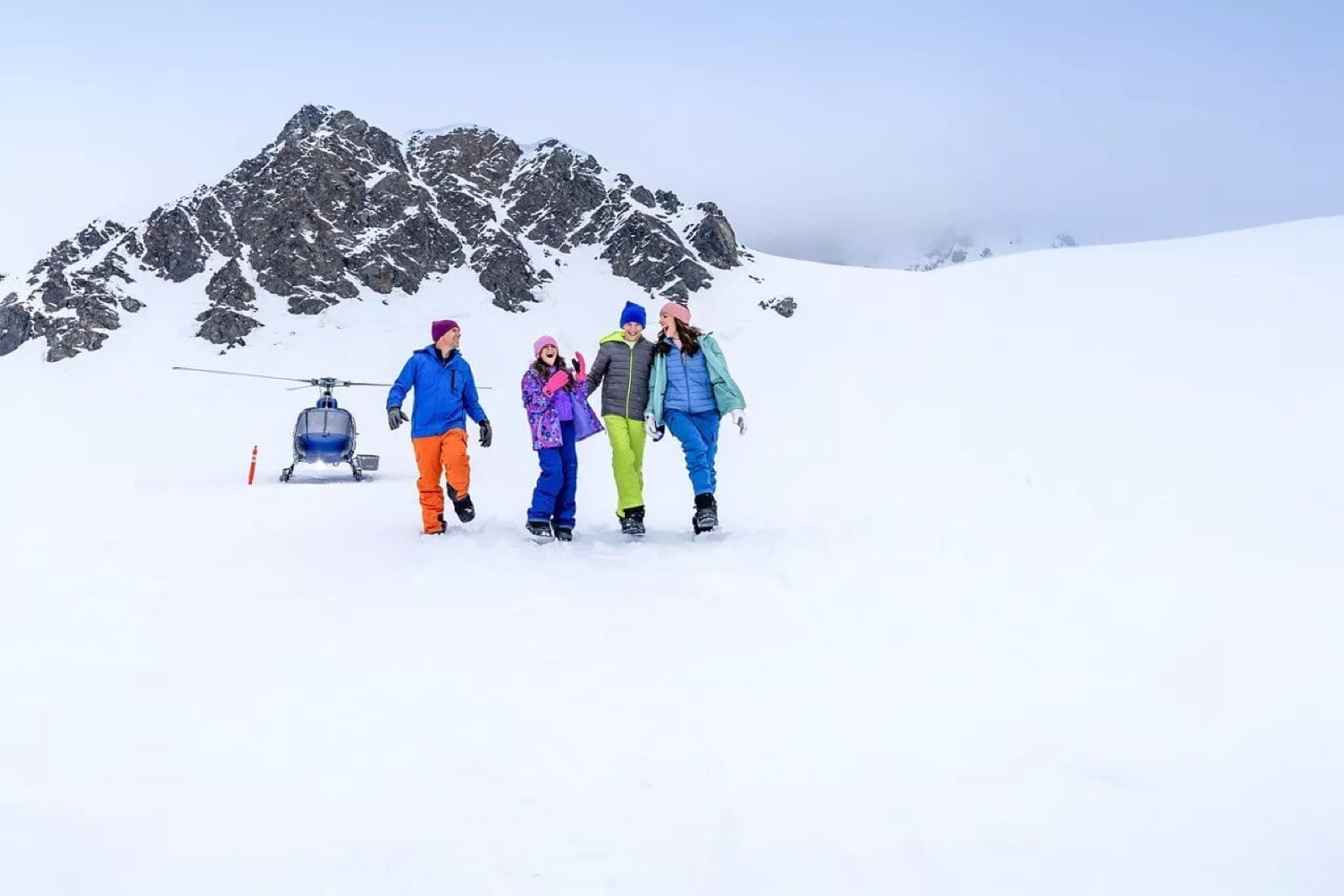 A family on an Alaskan glacier excursion with a helicopter and snow-capped peaks